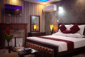Habitación de hotel con cama, lámparas de noche, televisor de pantalla plana, aire acondicionado, espejo y una mesa con un menú.