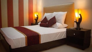 A bed with white bedding and a red throw, flanked by two nightstands with lamps, in a room with striped wallpaper. - Mall View Hotel Gulberg (Lahore)
