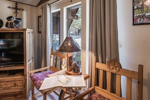 A cozy reading nook with a wooden chair, a table with a book and glasses, a lamp, and a television on a wooden cabinet. - Cowboys Indians And Outlaws By Vtrips (Ruidoso)