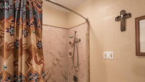 Ein Badezimmer mit Dusche, Waschbecken, Spiegel und einem an der Wand befestigten Kreuz.