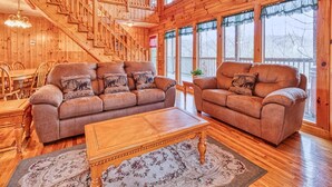 Ein geräumiges Holzhaus-Interieur mit einer Treppe, zwei Sofas mit passenden Kissen, einem Holztisch und einem großen Fenster mit Blick.