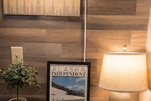 A framed newspaper with a mountainous landscape, a wall-mounted light fixture, and a potted plant.
