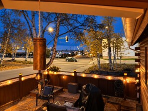 A covered outdoor area with a view of a street and trees, featuring a hanging light fixture and outdoor seating.
