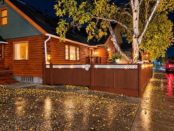 A wooden cabin with a porch, a tree, and a street with fallen leaves.