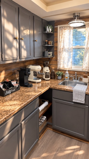 A kitchen with dark cabinets, a coffee maker, a sink, and a window with curtains.