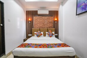 A hotel room with a bed, a headboard with a patterned design, two wall-mounted lights, and an air conditioning unit. - Fabhotel Sai Plaza Executive (Chhatrapati Sambhajinagar)