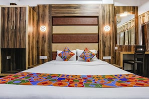 A bedroom with a bed, two pillows, a colorful rug, wooden panel walls, and a mirror. - Fabhotel Sai Plaza Executive (Chhatrapati Sambhajinagar)