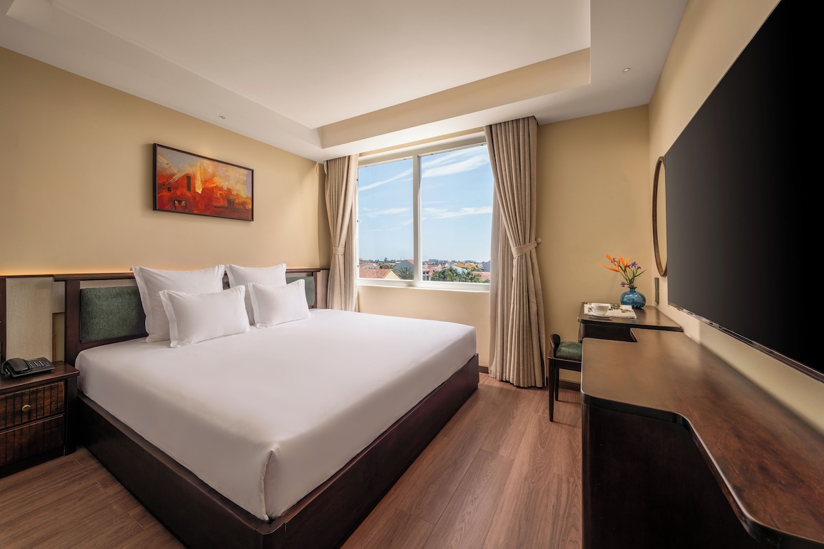 A hotel room with a large bed, a desk, a chair, a television, and a window with curtains.