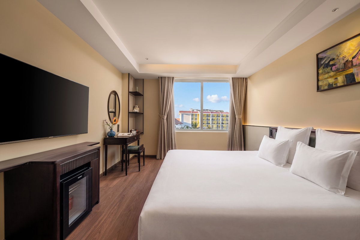 A hotel room with a large bed, a flat-screen TV, a desk with a chair, and a window with curtains.