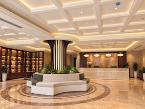 A hotel reception area with a curved seating arrangement, a reception desk, and a decorative column. - An Hoi Riverside Grand Hotel & Spa (Da Nang)