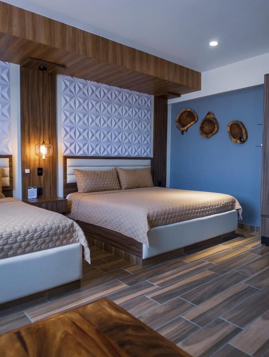 Habitación de hotel con dos camas, techo de madera, panel de pared geométrico y pared azul con detalles de madera.