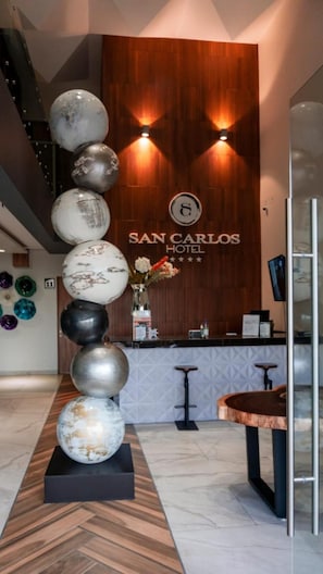 A reception area with a wooden wall, a reception desk, and a decorative glass sculpture. - Hotel San Carlos (La Barca)