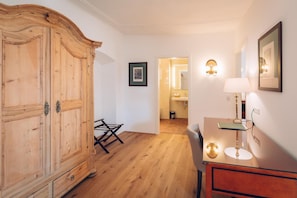 Una habitación con un armario de madera, un escritorio con lámpara, una silla y un cuadro en la pared.