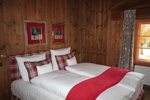 Una habitación con paneles de madera, una cama, dos cuadros en la pared y un ventanal con cortinas.