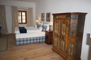 Un dormitorio con cama, mesita de noche, aparador de madera y ventana con cortinas.