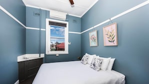 Een slaapkamer met een bed, een raam, een wandairconditioner, een wastafel en twee ingelijste foto's.