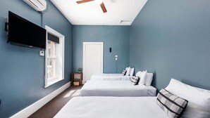 Een slaapkamer met twee bedden, een plafondventilator, een aan de muur bevestigde televisie en een raam.