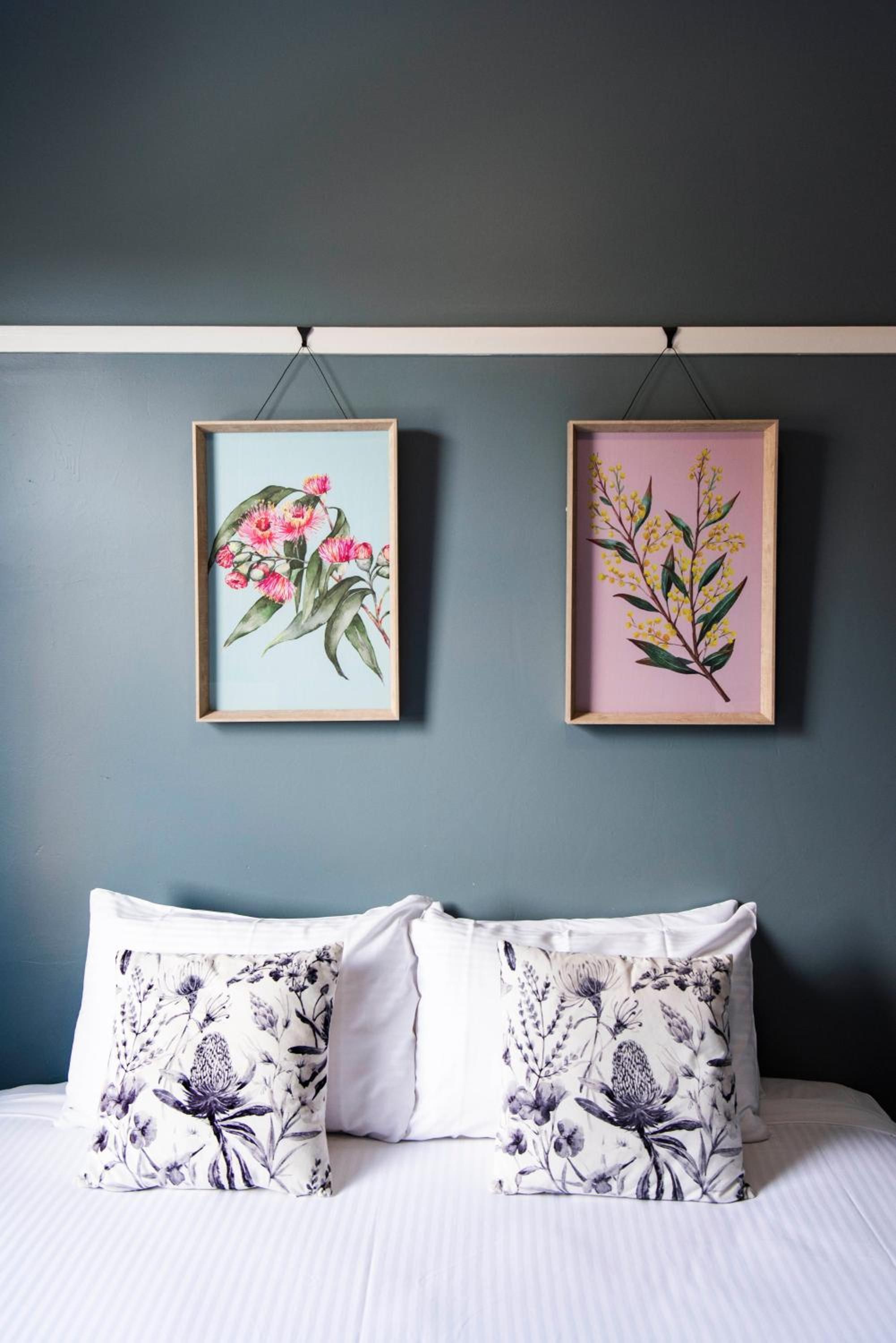 A bedroom with a bed, two pillows with floral patterns, and two framed botanical prints on the wall.