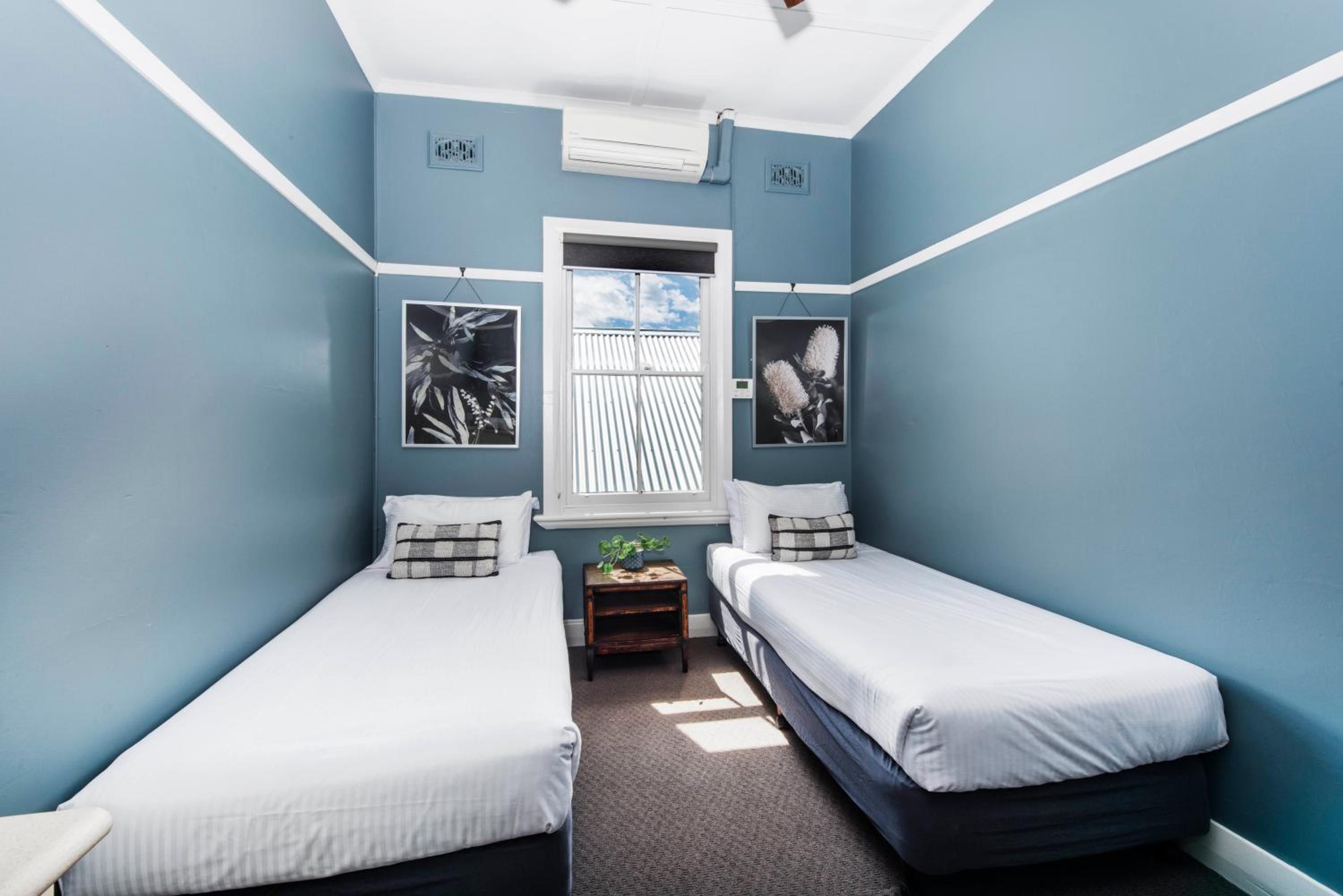 A room with two single beds, a window, and two wall-mounted pictures.