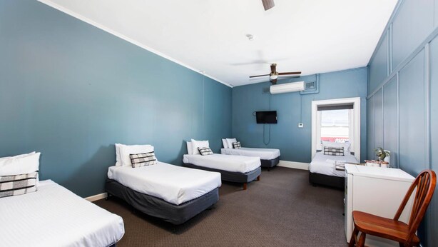 Een hotelkamer met drie bedden, een bureau, een stoel, een plafondventilator en een televisie.