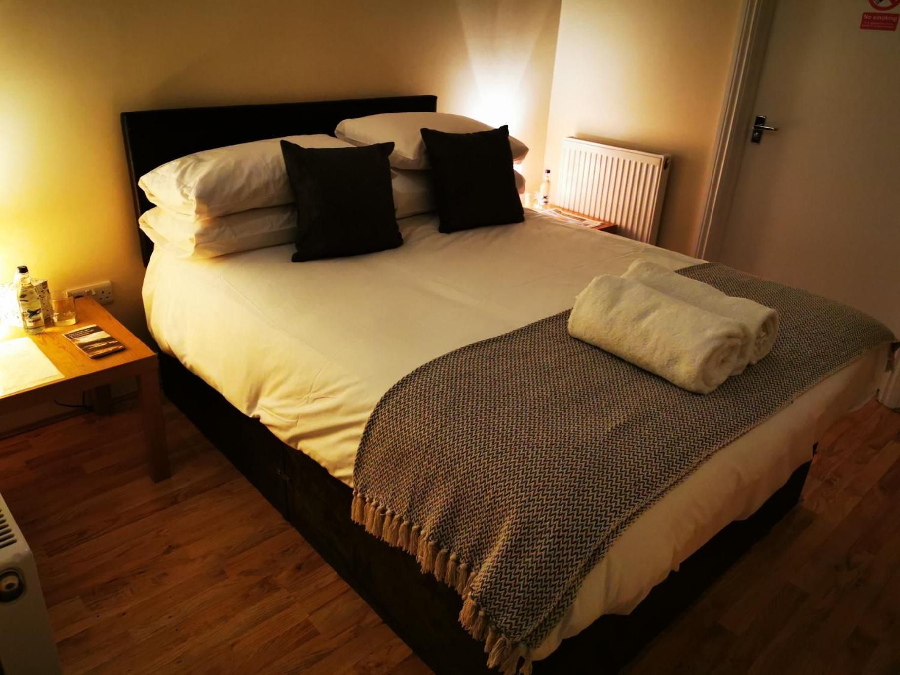 A neatly made bed with white linens, a dark headboard, and a patterned throw blanket.