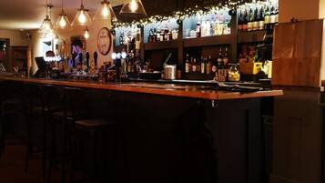 A bar area with multiple hanging light fixtures, a counter with bar stools, and shelves stocked with bottles.