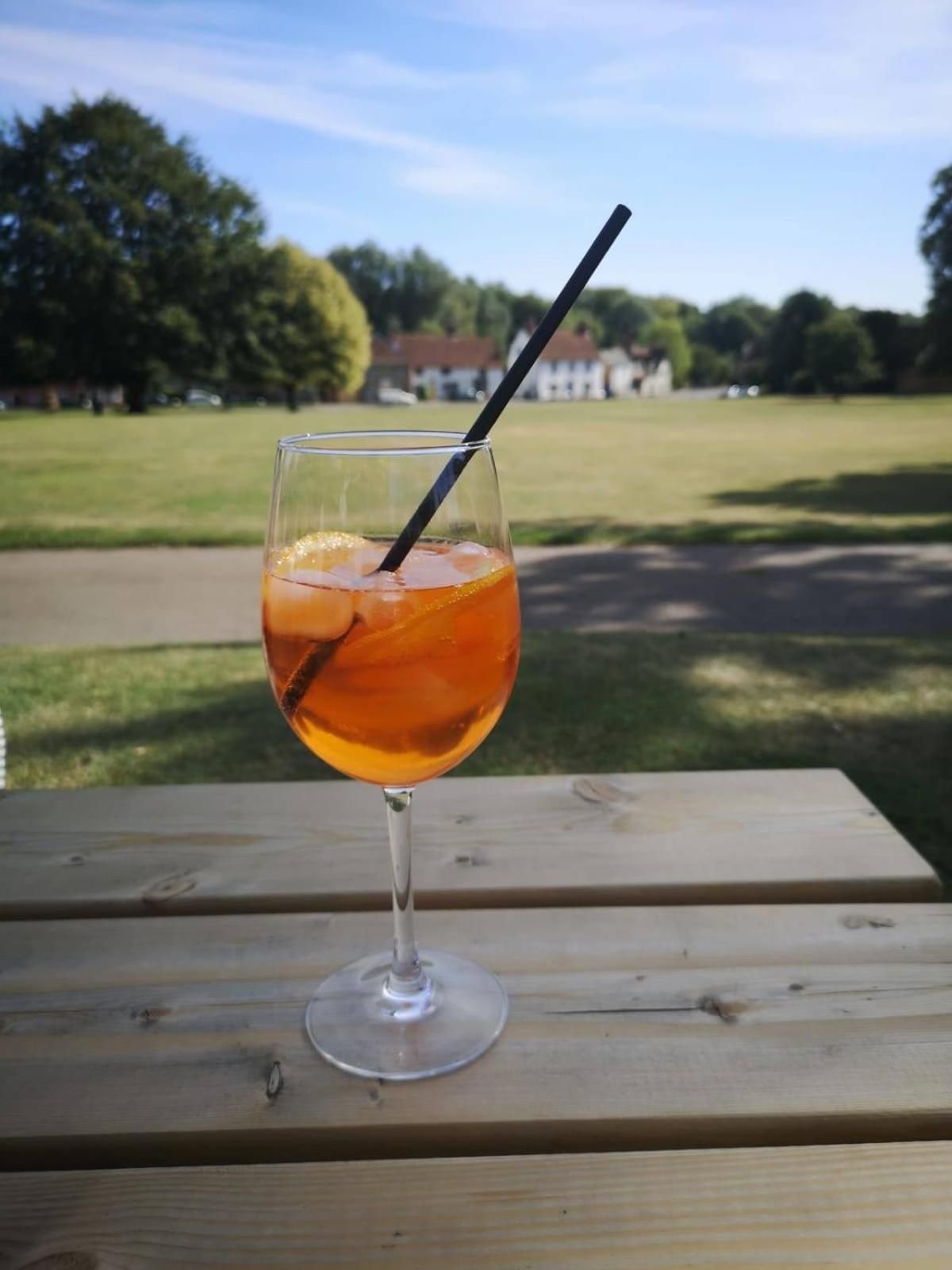 A glass of amber-colored beverage with a straw on a wooden table.