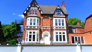 A two-story Victorian-style building with a prominent bay window, a central entrance with a decorative arch, and a brick facade. - The Elmsleigh Suite At Claremont Hotel (Nottingham)