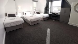 A modern hotel room with three beds, a desk, and a large window. - The Elmsleigh Suite At Claremont Hotel (Nottingham)