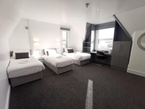 Ein modernes Hotelzimmer mit drei Betten, einem Schreibtisch und einem großen Fenster.