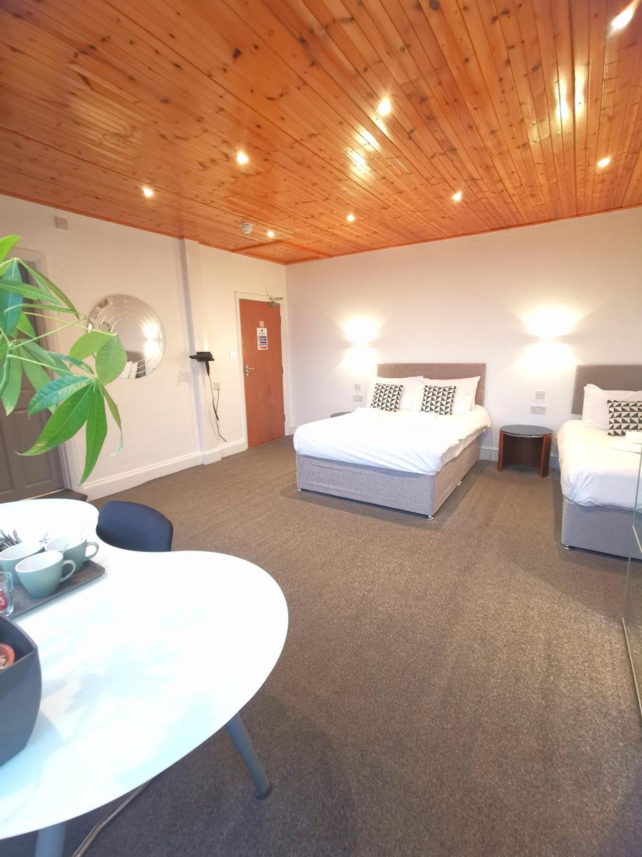 A hotel room with a wooden ceiling, a bed with pillows, a bedside table, a chair, and a round table with cups and a tray.