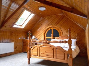 Ein Schlafzimmer im Dachgeschoss mit Holzboden und schrägen Wänden, einem Bett mit Holz Kopfteil, einem Schminktisch und einem Oberlicht.