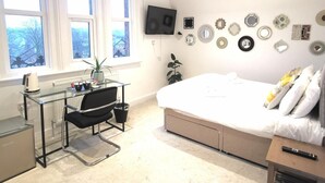 A modern bedroom with a large bed, a desk with a chair, a TV mounted on the wall, and a window with a view of trees. - The Elmsleigh Suite At Claremont Hotel (Nottingham)