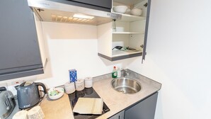 A compact kitchen with a built-in sink, a kettle, and a shelf with dishes. - Charming Studio In Birmingham (Birmingham)