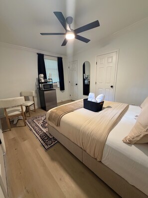 Ein Schlafzimmer mit einem Bett, einem Schreibtisch, einem Stuhl, einem Deckenventilator und einem Fenster mit Vorhängen.
