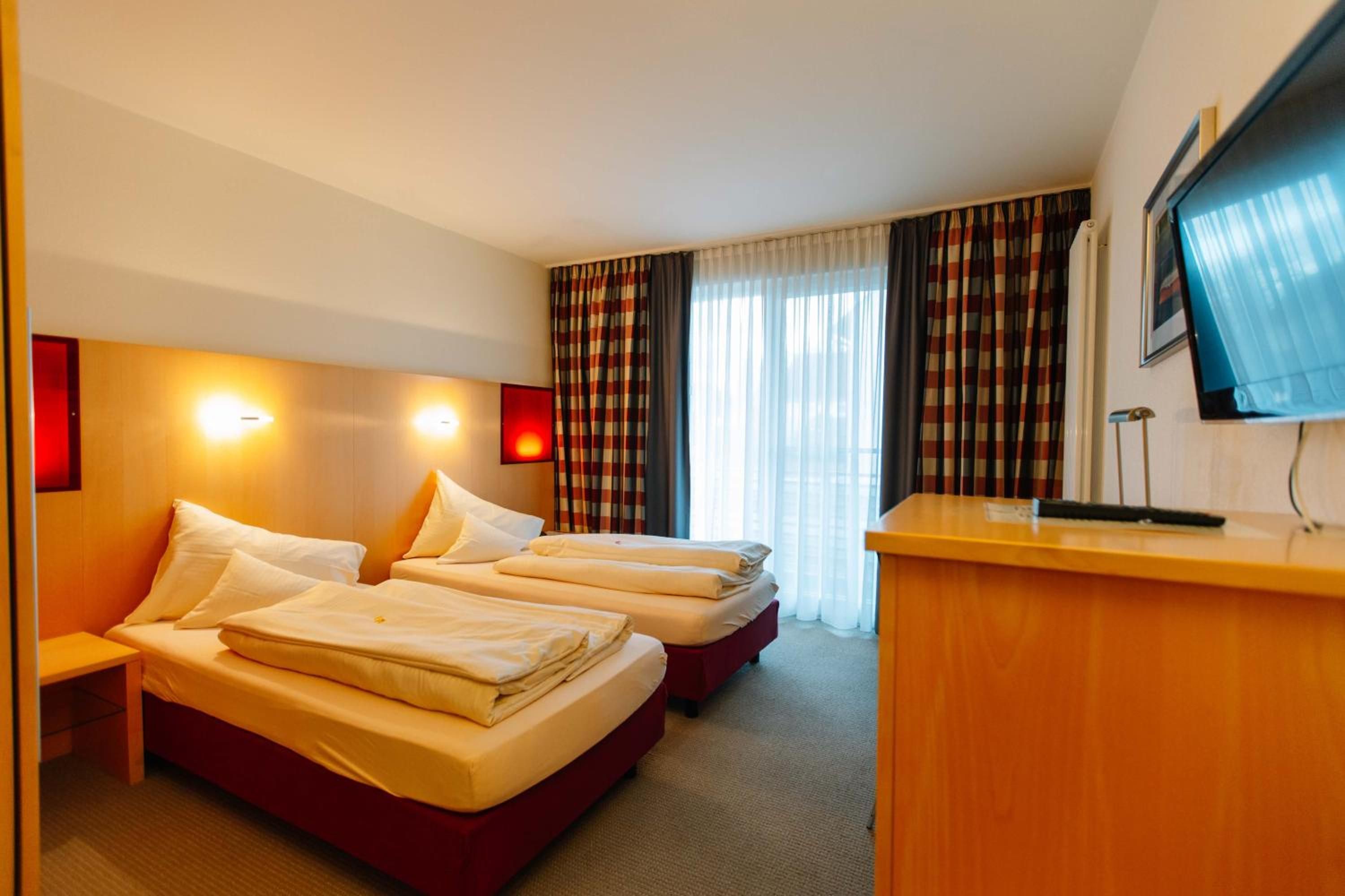 A hotel room with two beds, a desk, and a television.