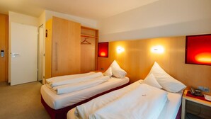 A hotel room with two beds, a wardrobe, a desk with a phone, and a wall-mounted light. - Landhotel Gasthof Drexler Gbr (Fuerstenfeldbruck)