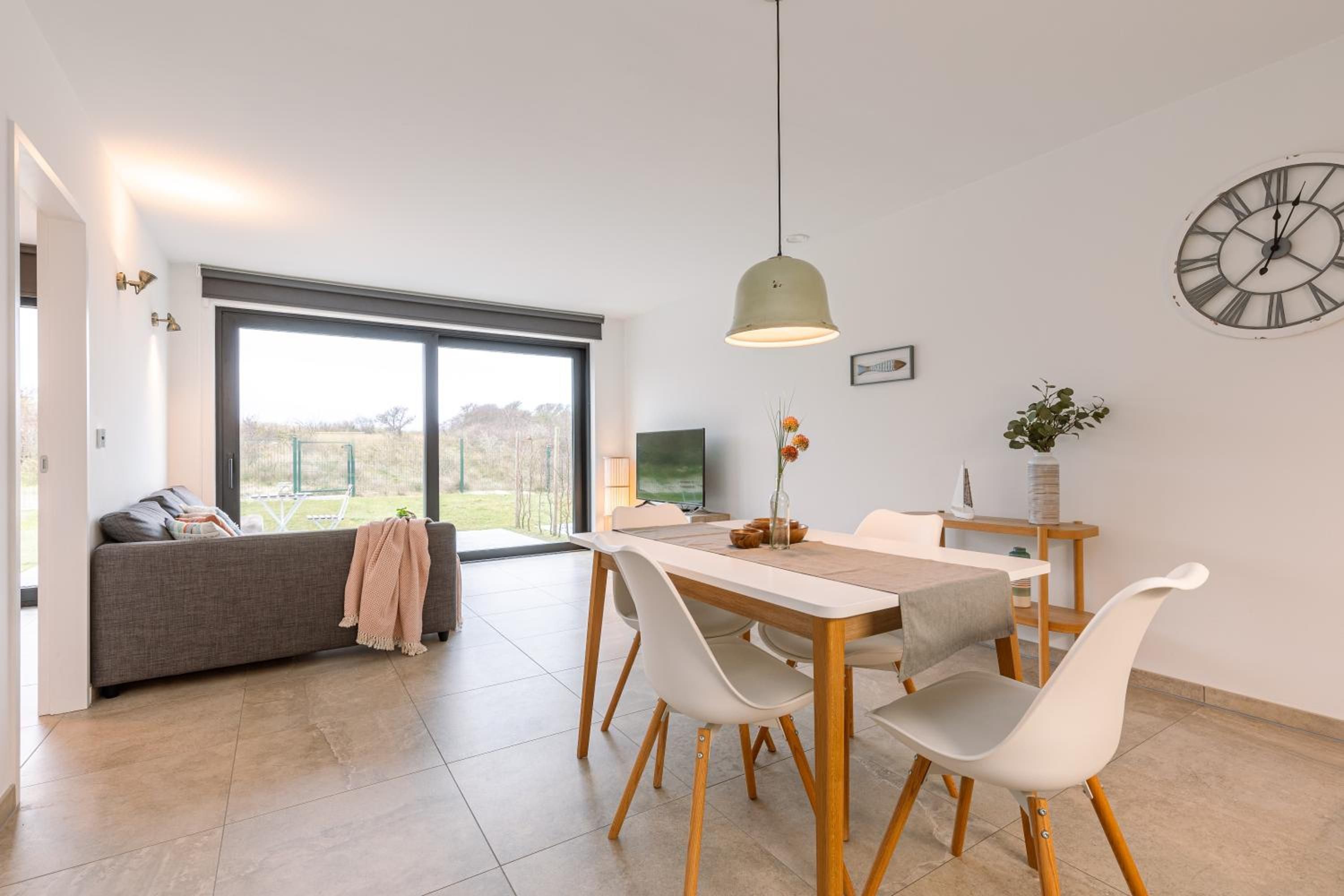 Een moderne woonruimte met een eethoek, een bank, een televisie en een groot raam met uitzicht op de omgeving.