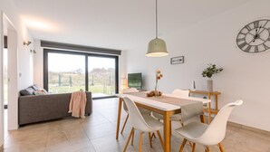 Un espacio de estar moderno con comedor, sofá, televisor y un amplio ventanal con vistas al exterior.