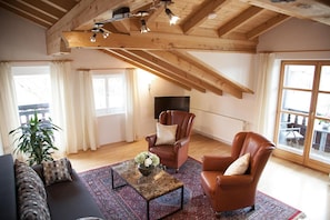 A spacious living room with a high ceiling, wooden beams, a large window, and a television. - Hotel Garni Georgenhof Adults Only (Rimsting)