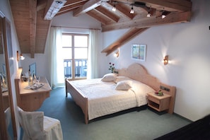 A bedroom with a wooden ceiling, a large bed with pillows, a bedside table with a lamp, and a window with curtains. - Hotel Garni Georgenhof Adults Only (Rimsting)