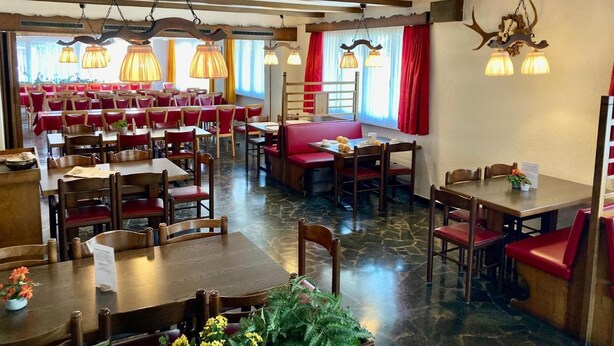 Un restaurant amb diverses taules i seients, sòls de pedra i il·luminació penjant.