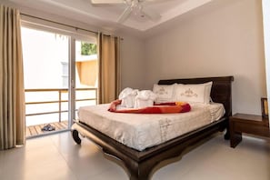 Una habitación de hotel con una cama, una mesita de noche, un ventilador de techo y un gran ventanal corredizo.