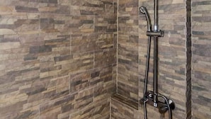 Een douchegedeelte met een regendouche en een handdouche, voor een wand met een tegelpatroon dat op steen lijkt.