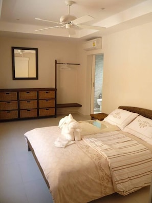 Un dormitorio con cama, ventilador de techo, armario y baño visible a través de una puerta abierta.