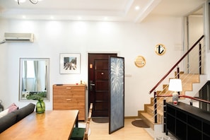 A modern living room with a wooden dining table, a sofa, and a staircase leading to an upper floor. - Innocondo Extended Stay Changning Yuyuan (Shanghai)