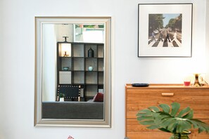 A mirror with a metallic frame, a framed picture on the wall, a wooden dresser, and a plant.