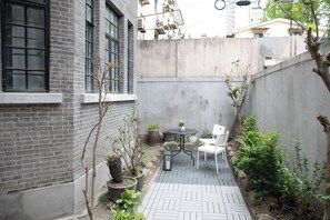 Un petit patio extérieur, avec un mur en briques, une petite table ronde et deux chaises.