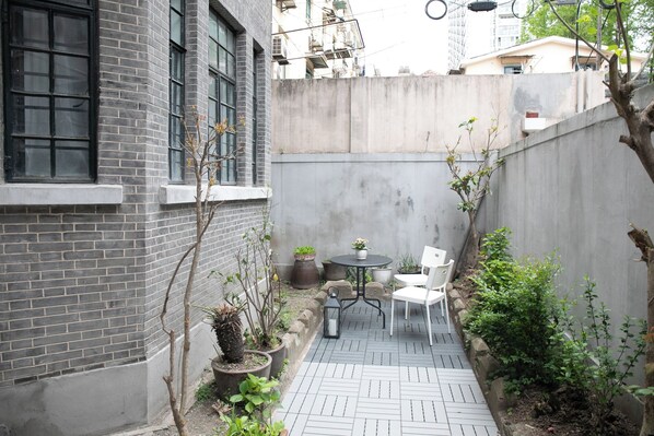 A narrow outdoor patio with a brick wall, a small round table, and two chairs. - Innocondo Extended Stay Changning Yuyuan (Shanghai)