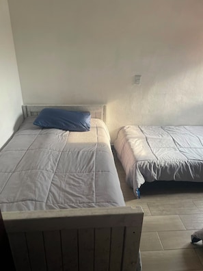 Quarto com duas camas, cada uma com cabeceira e travesseiro. As camas estão cobertas com roupa de cama em tons claros.